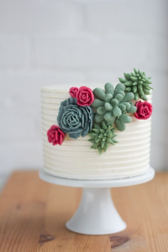 white cake with some succulents and red flowers in butter cream on the side