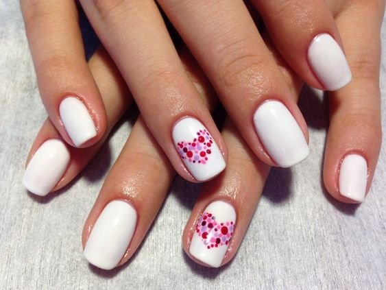 white nails and hearts drawn in pink polka dots on 2 fingers