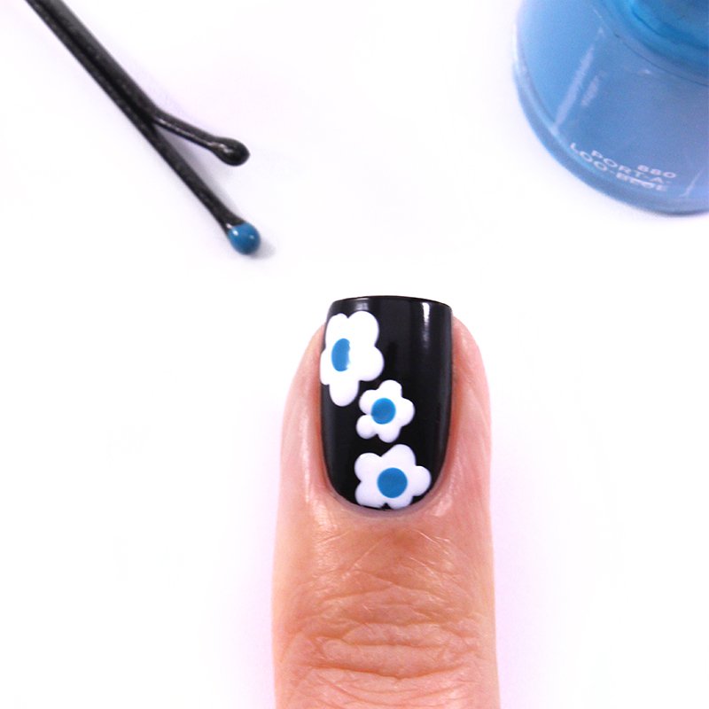 3 small white flowers with blue heart on nail varnish in black